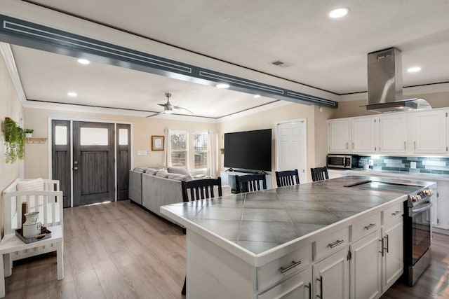 kitchen with island exhaust hood, tile countertops, crown molding, stainless steel appliances, and white cabinetry