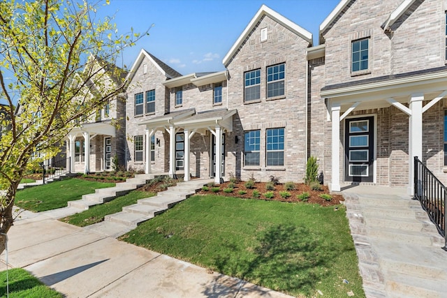 townhome / multi-family property with covered porch, a front lawn, and brick siding