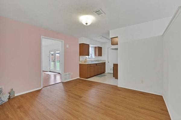 unfurnished living room with light wood-type flooring, visible vents, a sink, and baseboards