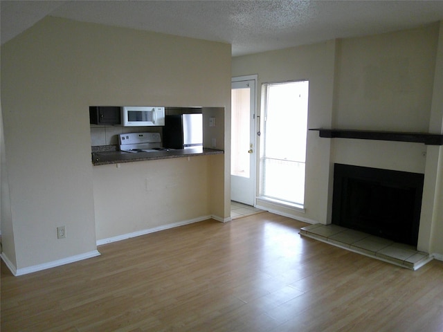 kitchen with white microwave, stove, a fireplace, freestanding refrigerator, and light wood finished floors