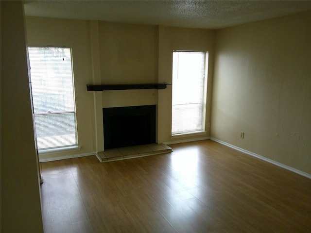 unfurnished living room with a wealth of natural light, a fireplace, a textured ceiling, and wood finished floors