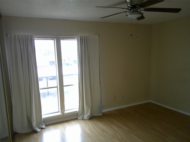 unfurnished room with a textured ceiling, ceiling fan, light wood-style flooring, and baseboards