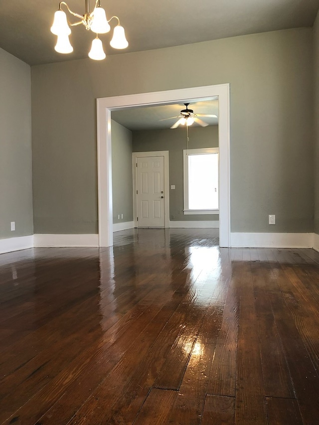 unfurnished living room with dark wood-type flooring, baseboards, and ceiling fan with notable chandelier