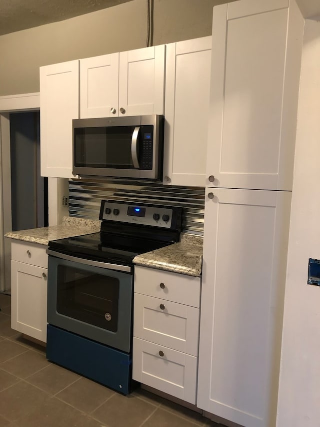 kitchen with stainless steel appliances, dark tile patterned floors, white cabinetry, and light stone counters