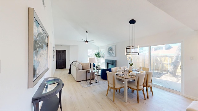 dining space featuring light wood-type flooring, high vaulted ceiling, a ceiling fan, and a glass covered fireplace