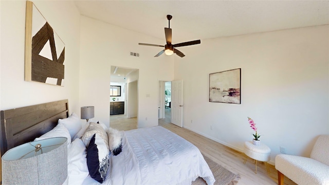 bedroom featuring ensuite bathroom, a high ceiling, visible vents, baseboards, and light wood-style floors