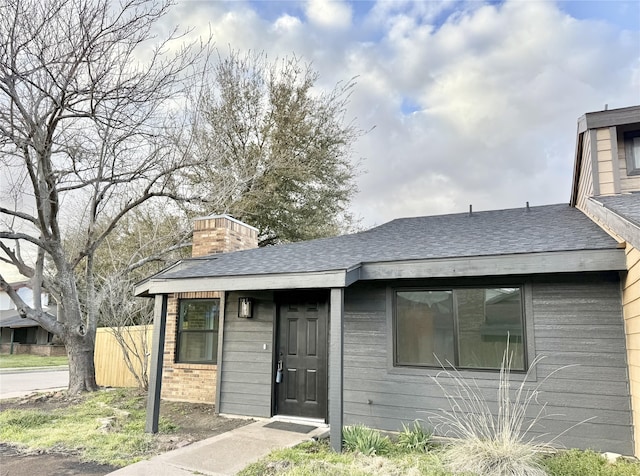 view of front of house with roof with shingles, brick siding, a chimney, and fence