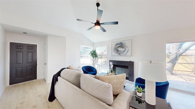 living area with light wood-style flooring, vaulted ceiling, a ceiling fan, and a glass covered fireplace