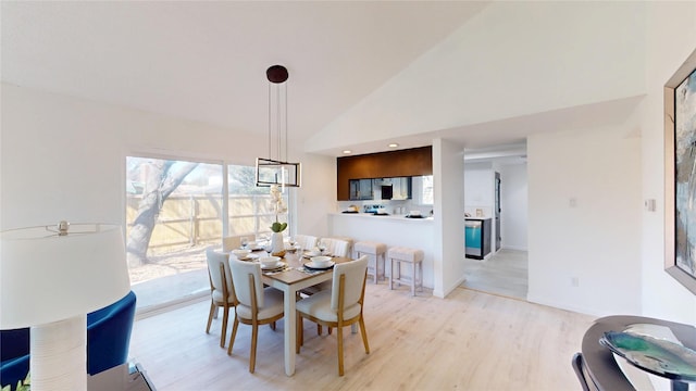 dining space featuring light wood finished floors, baseboards, and high vaulted ceiling