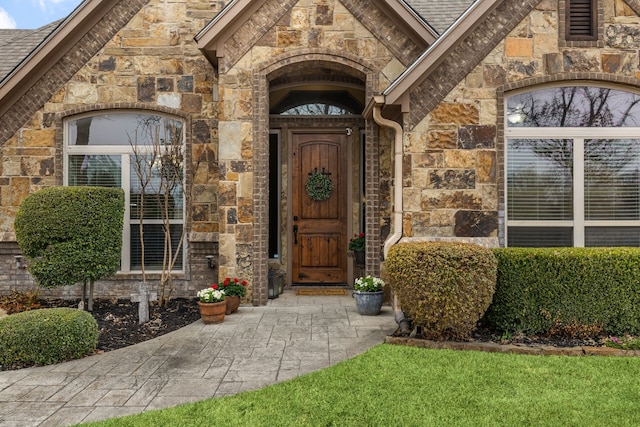 view of exterior entry featuring stone siding, a shingled roof, and brick siding