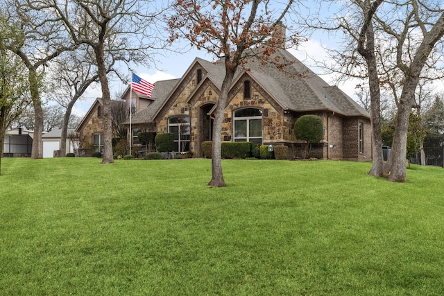 view of front of home featuring stone siding, a chimney, a front lawn, and roof with shingles