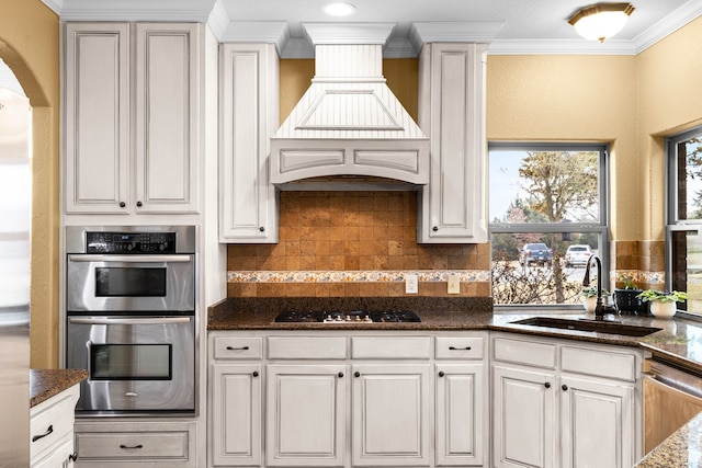 kitchen with white cabinets, ornamental molding, stainless steel appliances, premium range hood, and a sink