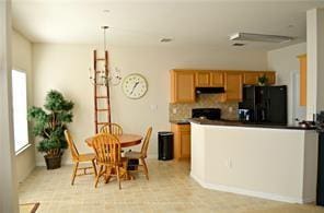 kitchen featuring dark countertops, decorative backsplash, freestanding refrigerator, a peninsula, and under cabinet range hood