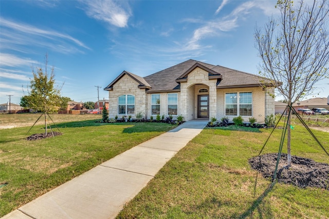 french provincial home featuring a shingled roof, stone siding, fence, a front yard, and brick siding