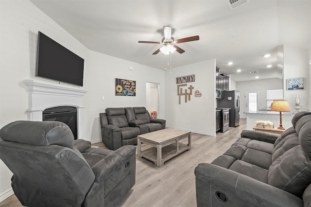 living area featuring light wood finished floors, recessed lighting, a ceiling fan, a glass covered fireplace, and baseboards