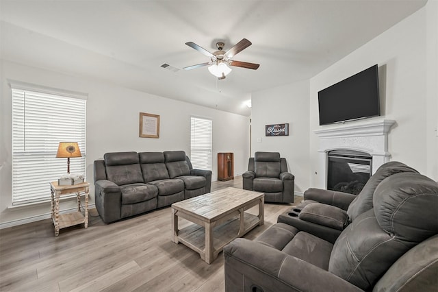 living room with baseboards, visible vents, a ceiling fan, a glass covered fireplace, and light wood-style flooring