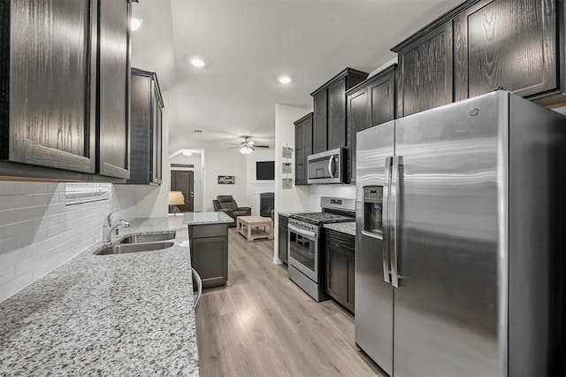 kitchen featuring stainless steel appliances, a sink, light wood-style floors, open floor plan, and decorative backsplash