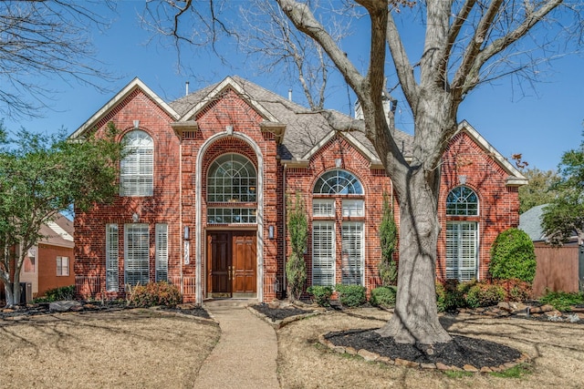 traditional-style home featuring a shingled roof and brick siding