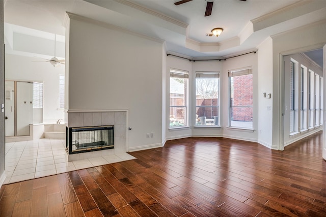 unfurnished living room featuring a tray ceiling, ceiling fan, and wood finished floors