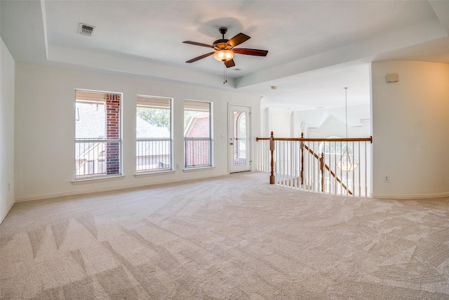 empty room with carpet floors, a tray ceiling, visible vents, and ceiling fan