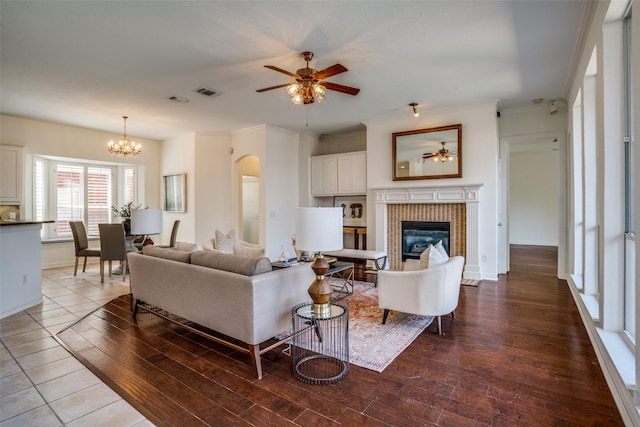 living room featuring crown molding, a fireplace, visible vents, wood finished floors, and ceiling fan with notable chandelier