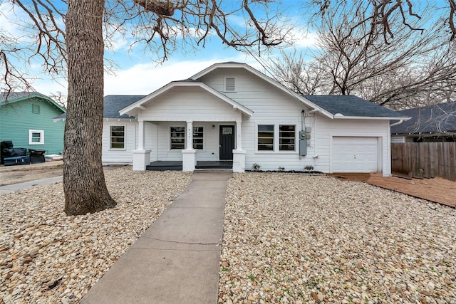 view of front of home with covered porch, roof with shingles, fence, and a garage