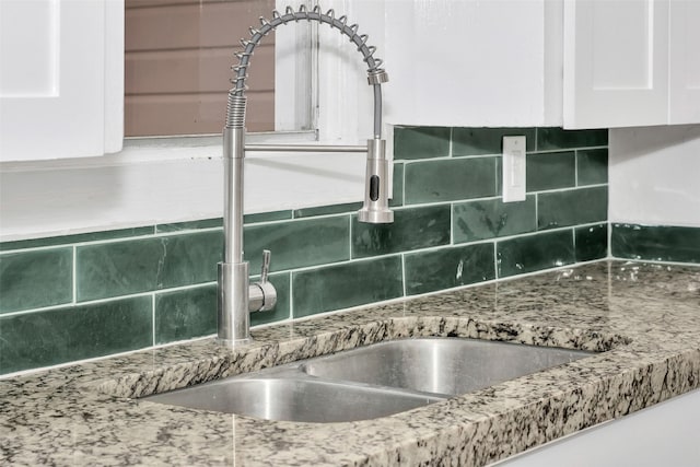 details with tasteful backsplash, stone counters, a sink, and white cabinets