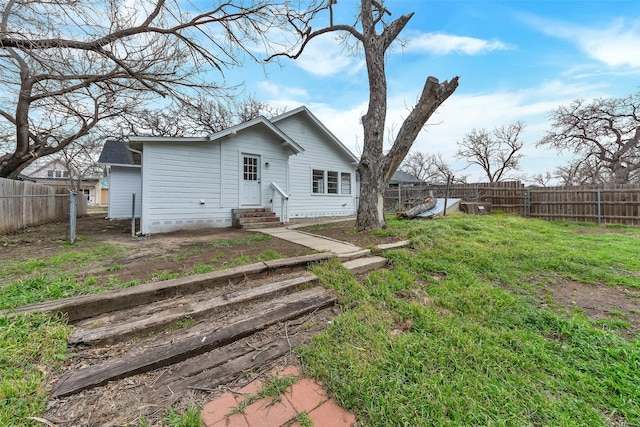 rear view of house featuring entry steps, a fenced backyard, and a yard