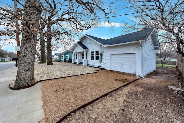 view of front of property with dirt driveway, roof with shingles, an attached garage, and fence