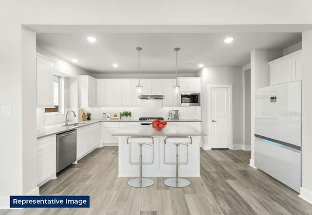 kitchen with decorative backsplash, a kitchen island, a sink, white cabinets, and stainless steel appliances