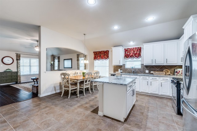 kitchen featuring arched walkways, stainless steel appliances, white cabinetry, vaulted ceiling, and tasteful backsplash