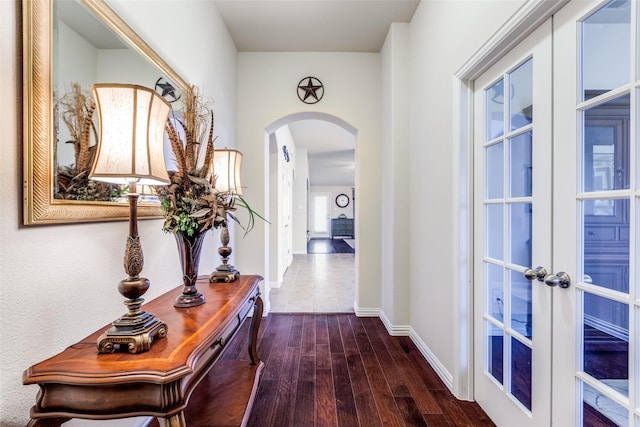 corridor featuring arched walkways, baseboards, and wood finished floors