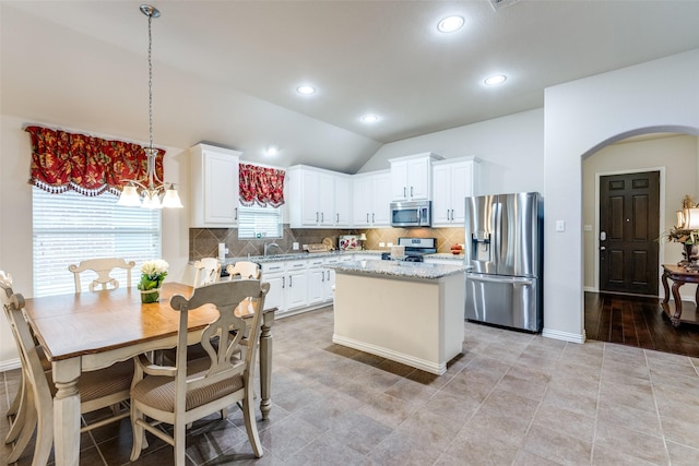 kitchen featuring arched walkways, appliances with stainless steel finishes, white cabinets, and tasteful backsplash