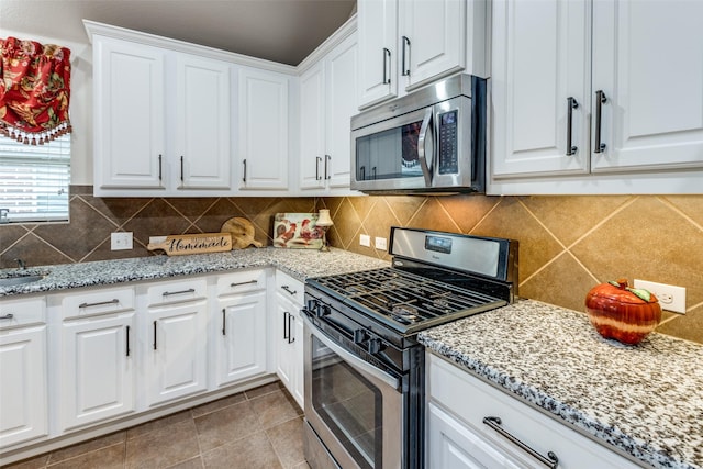 kitchen with stainless steel appliances, tasteful backsplash, white cabinetry, and light stone countertops