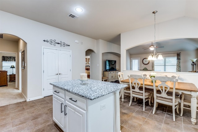 kitchen with visible vents, arched walkways, light stone counters, a center island, and vaulted ceiling