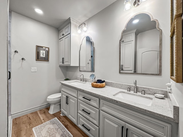 full bathroom with toilet, double vanity, a sink, and wood finished floors