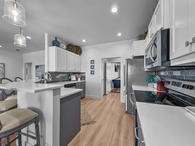 kitchen with white cabinets, a peninsula, stainless steel appliances, light wood-type flooring, and a kitchen bar