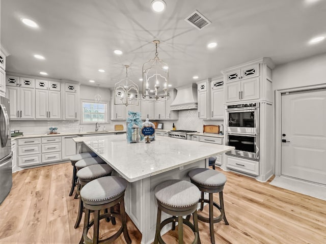 kitchen with stainless steel appliances, premium range hood, a kitchen island, a sink, and visible vents