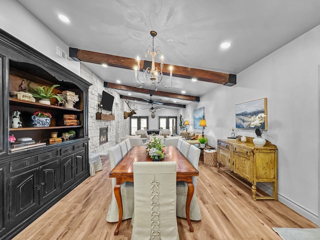 dining area featuring light wood finished floors, a stone fireplace, beam ceiling, and visible vents