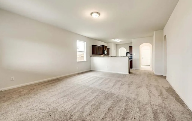 unfurnished living room featuring arched walkways, light colored carpet, and baseboards