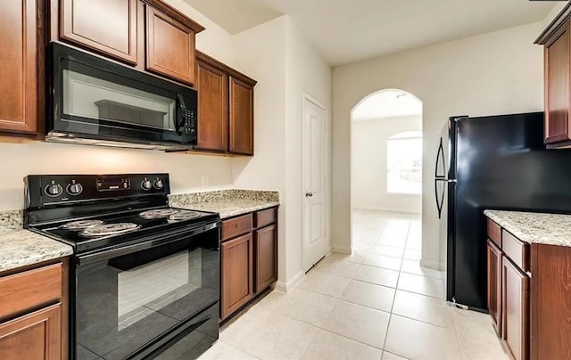 kitchen featuring arched walkways, light tile patterned floors, black appliances, light stone countertops, and baseboards