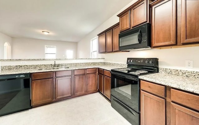 kitchen featuring light tile patterned floors, black appliances, light stone counters, and a sink