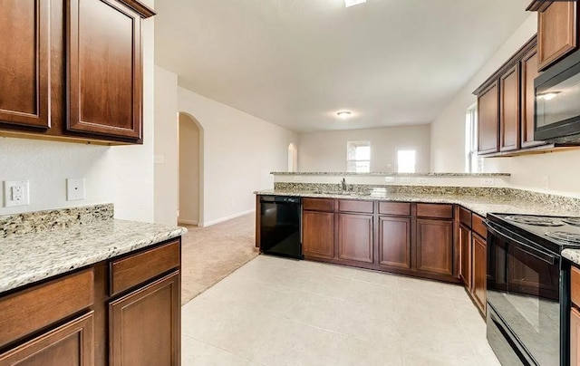 kitchen with arched walkways, a peninsula, a sink, light stone countertops, and black appliances