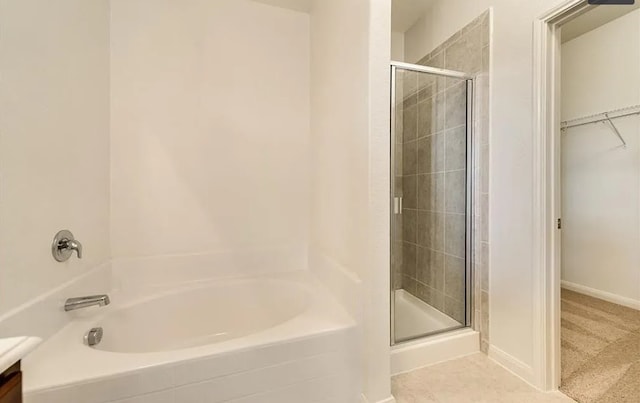 full bathroom featuring a walk in closet, a garden tub, a stall shower, vanity, and baseboards