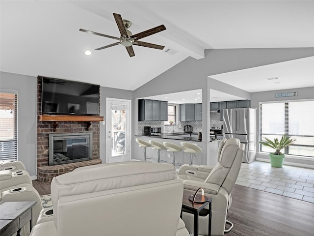 living area with lofted ceiling with beams, a brick fireplace, visible vents, and wood finished floors