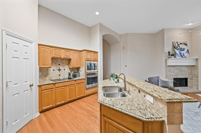 kitchen featuring tasteful backsplash, appliances with stainless steel finishes, light wood-style floors, a fireplace, and a sink