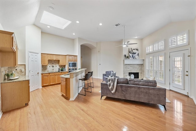 living area with light wood-type flooring, high vaulted ceiling, visible vents, and a stone fireplace