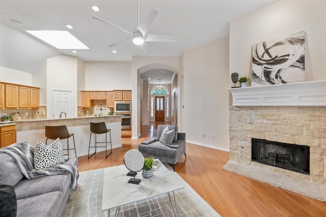 living room with arched walkways, a fireplace, a ceiling fan, vaulted ceiling, and light wood finished floors