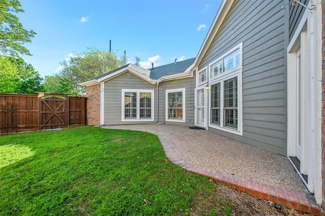 rear view of property featuring brick siding, fence, a yard, a gate, and a patio area