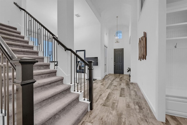 entryway featuring visible vents, baseboards, stairs, a towering ceiling, and light wood-type flooring